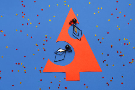 Paper Christmas tree with earrings and confetti on blue backgroundの写真素材