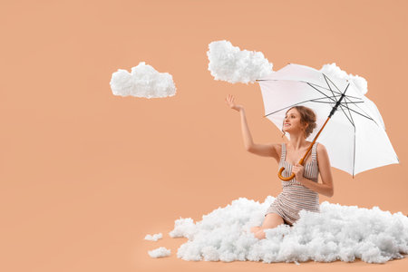 Young woman with umbrella and white clouds on beige backgroundの写真素材