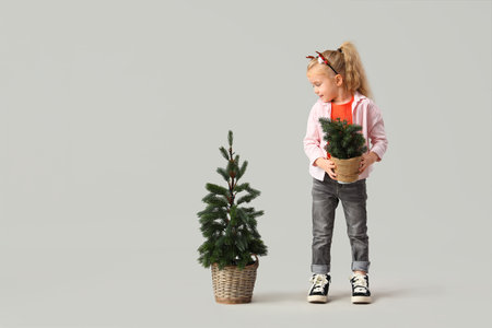 Cute little girl with Christmas trees on light backgroundの写真素材