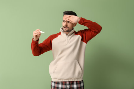 Sick young man with thermometer on green backgroundの写真素材