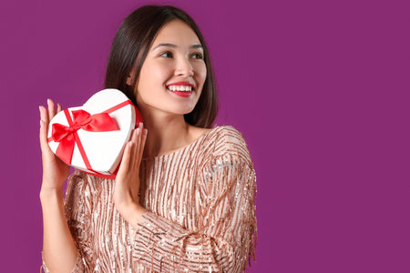 Beautiful young Asian woman with gift box for Valentine's Day on purple backgroundの写真素材