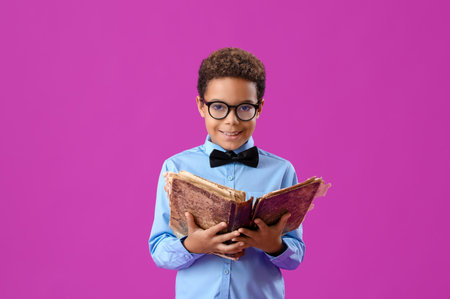 Little African-American boy with old book on purple background