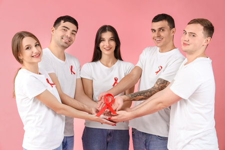 Group of young people with red ribbons on pink background. World AIDS day concept