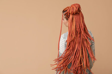 Young woman with dreadlocks on beige background, back view