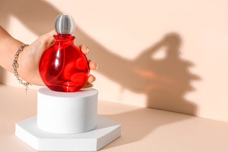 Female hand with bottle of elegant perfume on stands against beige backgroundの写真素材