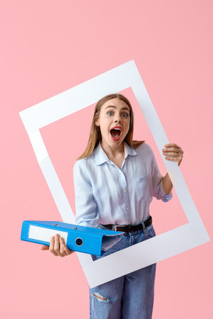 Surprised young businesswoman with document folder and frame on pink backgroundの写真素材