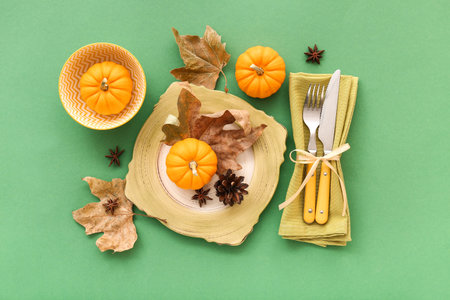 Autumn table setting with pumpkins, star anise and dried leaves on green background