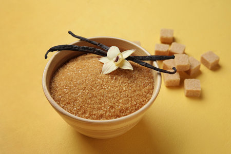 Bowl with aromatic vanilla sugar, flower and sticks on yellow backgroundの写真素材