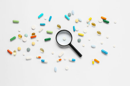 Fish oil capsules with different pills and magnifying glass on white background