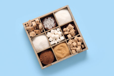 Wooden box with different types of sugar on blue background