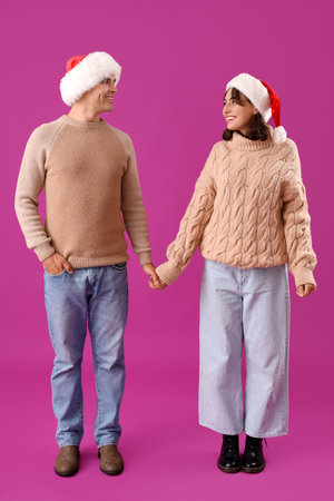 Happy young couple in Santa hats on purple backgroundの写真素材