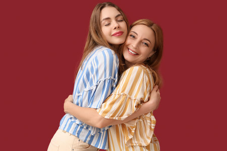 Beautiful young woman hugging her happy mother on red background. International Hug Day