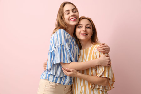 Happy young woman hugging her mother on pink background. International Hug Day