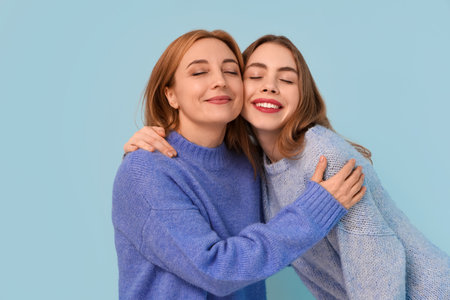 Mature woman hugging her happy young daughter on blue background. International Hug Dayの写真素材