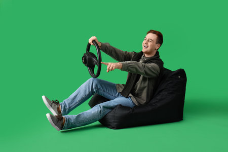 Young man with steering wheel pointing at something on green backgroundの写真素材