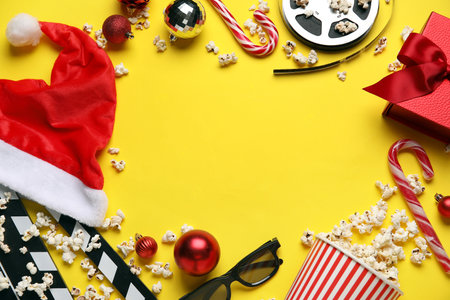 Frame made of bucket of popcorn with 3D glasses, movie clapper and Christmas decor on yellow backgroundの写真素材