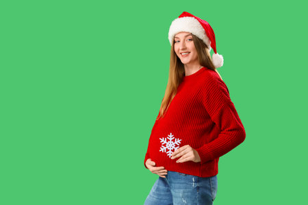 Beautiful young pregnant woman in Santa hat with snowflake on green backgroundの写真素材
