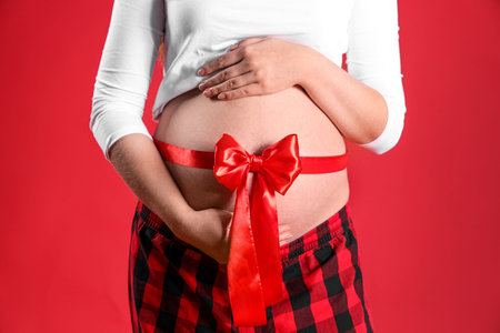 Beautiful young pregnant woman with ribbon around her waist on red background