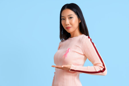 Young Asian woman with pink ribbon on blue background. Breast cancer awareness conceptの写真素材
