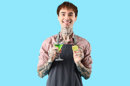 Young male bartender with glass of cocktail and lime on blue backgroundの写真素材