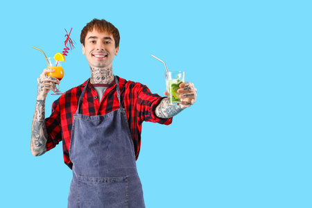 Young male bartender with glasses of cocktail on blue backgroundの写真素材