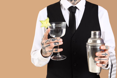 Male bartender with glass of cocktail and shaker on beige backgroundの写真素材