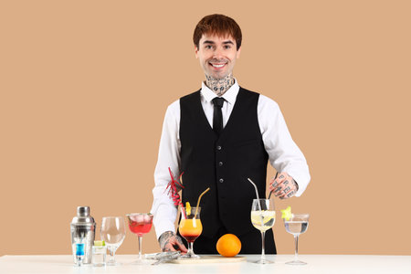 Young male bartender with cocktails at table on beige backgroundの写真素材