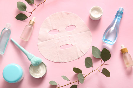 Facial sheet mask with different cosmetic products and leaves on pink backgroundの写真素材