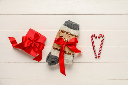 Knitted socks with Christmas gift box and candy canes on white wooden backgroundの写真素材