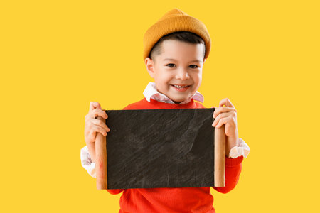 Little Asian boy with chalkboard on yellow backgroundの写真素材
