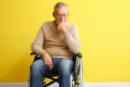 Thoughtful senior man in wheelchair near yellow wallの写真素材