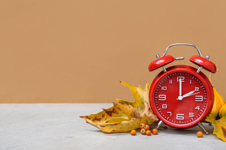 Alarm clock with autumn leaves and viburnum on gray table