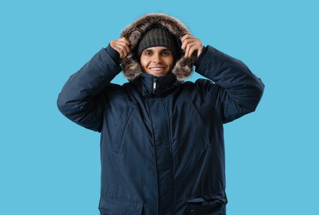 Young man in warm parka on blue background