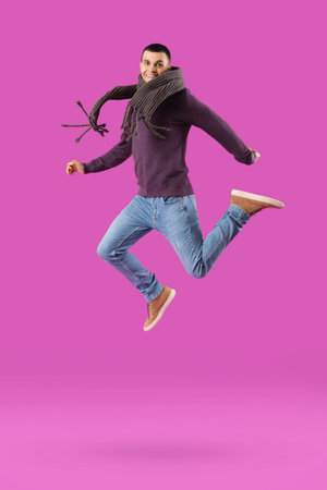Young man in winter clothes jumping on purple backgroundの写真素材
