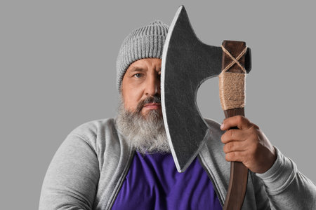 Portrait of mature man covering face with ax on gray backgroundの写真素材