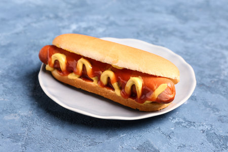 Plate with tasty hot dog on blue backgroundの写真素材
