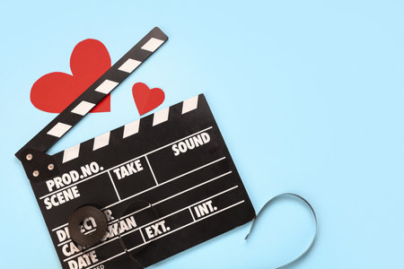 Movie clapper with film reel and paper hearts on blue background. Valentine's Day celebrationの写真素材