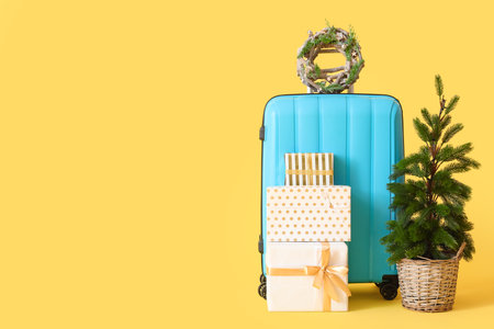 Suitcase with Christmas wreath, fir tree and presents on yellow backgroundの写真素材