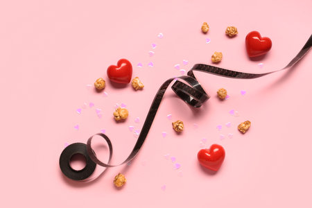 Film reel, popcorn and hearts on pink background. Valentine's Day celebration