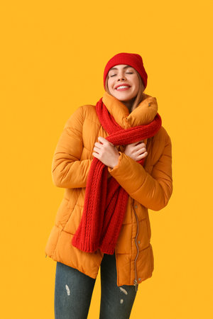 Beautiful young happy woman in warm winter clothes on yellow backgroundの写真素材