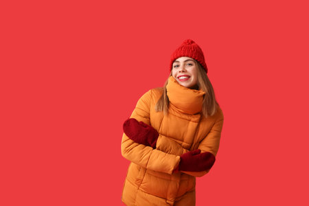 Beautiful young happy woman in warm winter clothes on red backgroundの写真素材