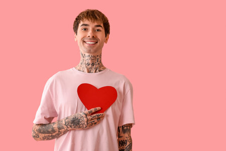 Happy young man with red paper heart on pink backgroundの写真素材