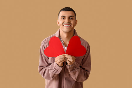 Happy young man with red paper hearts on brown backgroundの写真素材