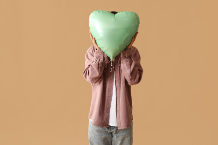 Young man with heart shaped air balloon on brown background