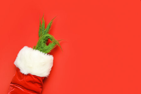 Green hairy hand of creature in Santa costume showing OK gesture on red background