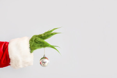 Green hairy hand of creature in Santa costume with Christmas ball on gray backgroundの写真素材