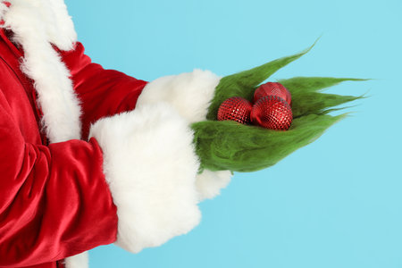 Green hairy hands of creature in Santa costume with Christmas balls on blue backgroundの写真素材