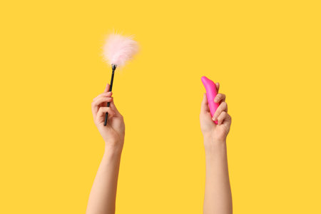Female hands with sex toys on yellow backgroundの写真素材