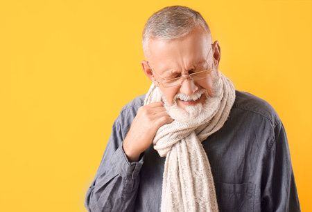 Sick mature man in scarf on yellow background, closeupの写真素材