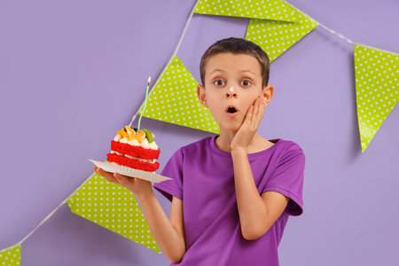 Cute shocked little boy with Birthday cake and garland on purple backgroundの写真素材